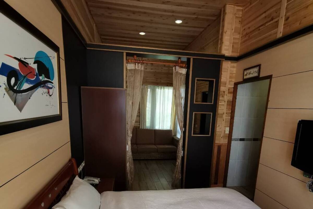 A bedroom with a bed, a wooden ceiling, a wall-mounted TV, and a painting.