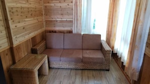 A wooden cabin interior with a sofa, a small table, and a window with curtains. - Dream Town (Ren'ai)