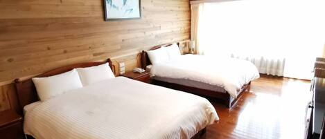 Habitación de hotel con dos camas, pisos de madera, cabecera de madera, un cuadro enmarcado en la pared y un ventanal grande.