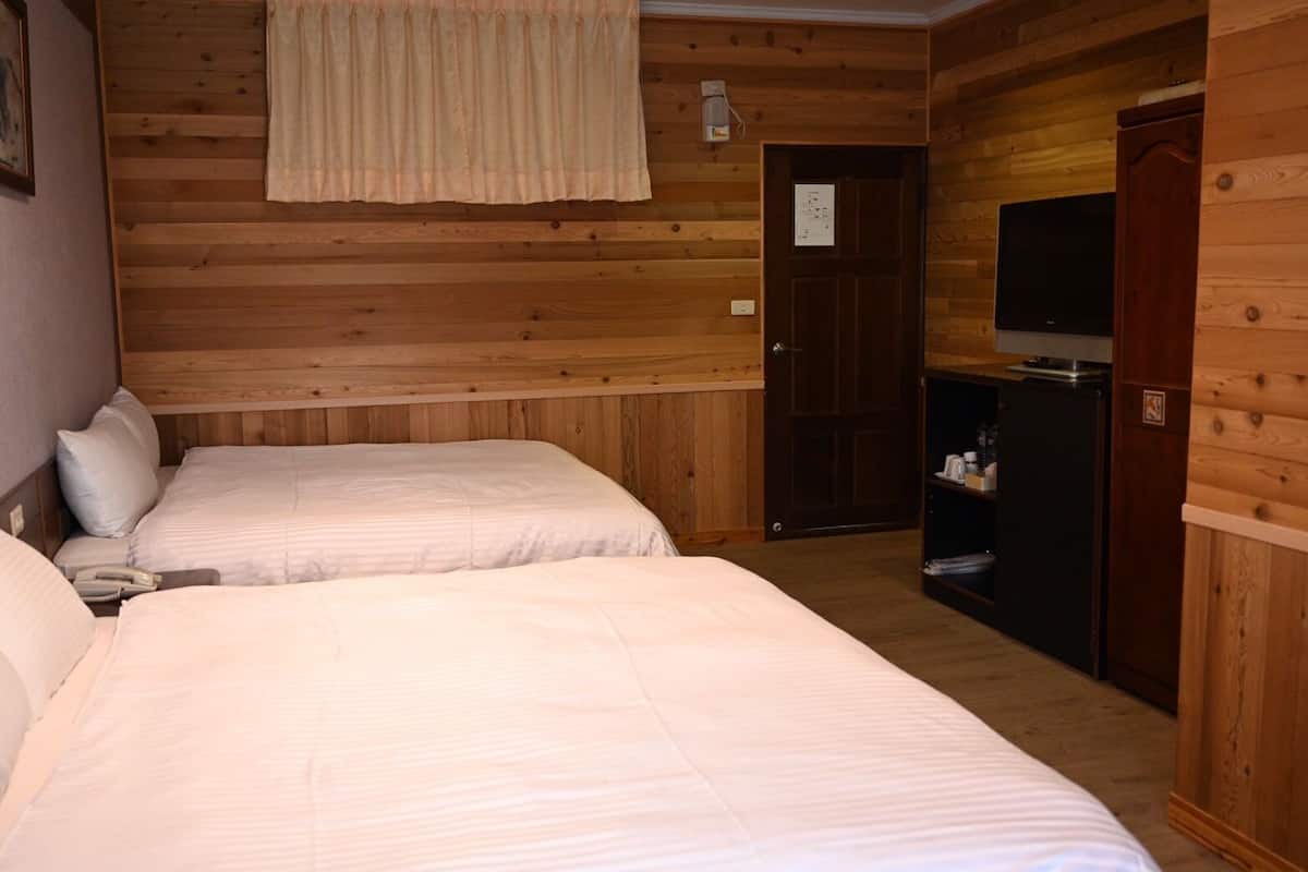 A room with two beds, a television, a wardrobe, and a door leading to another room.