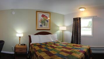 A hotel room with a bed, a nightstand with a lamp, a painting on the wall, and a window with curtains.