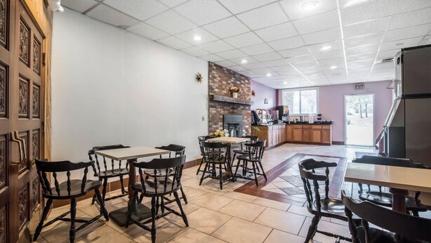 A spacious dining area with multiple tables and chairs, a kitchen area with a brick backsplash, and an exit sign on the wall. - Rodeway Inn Bellows Falls (Bellows Falls)