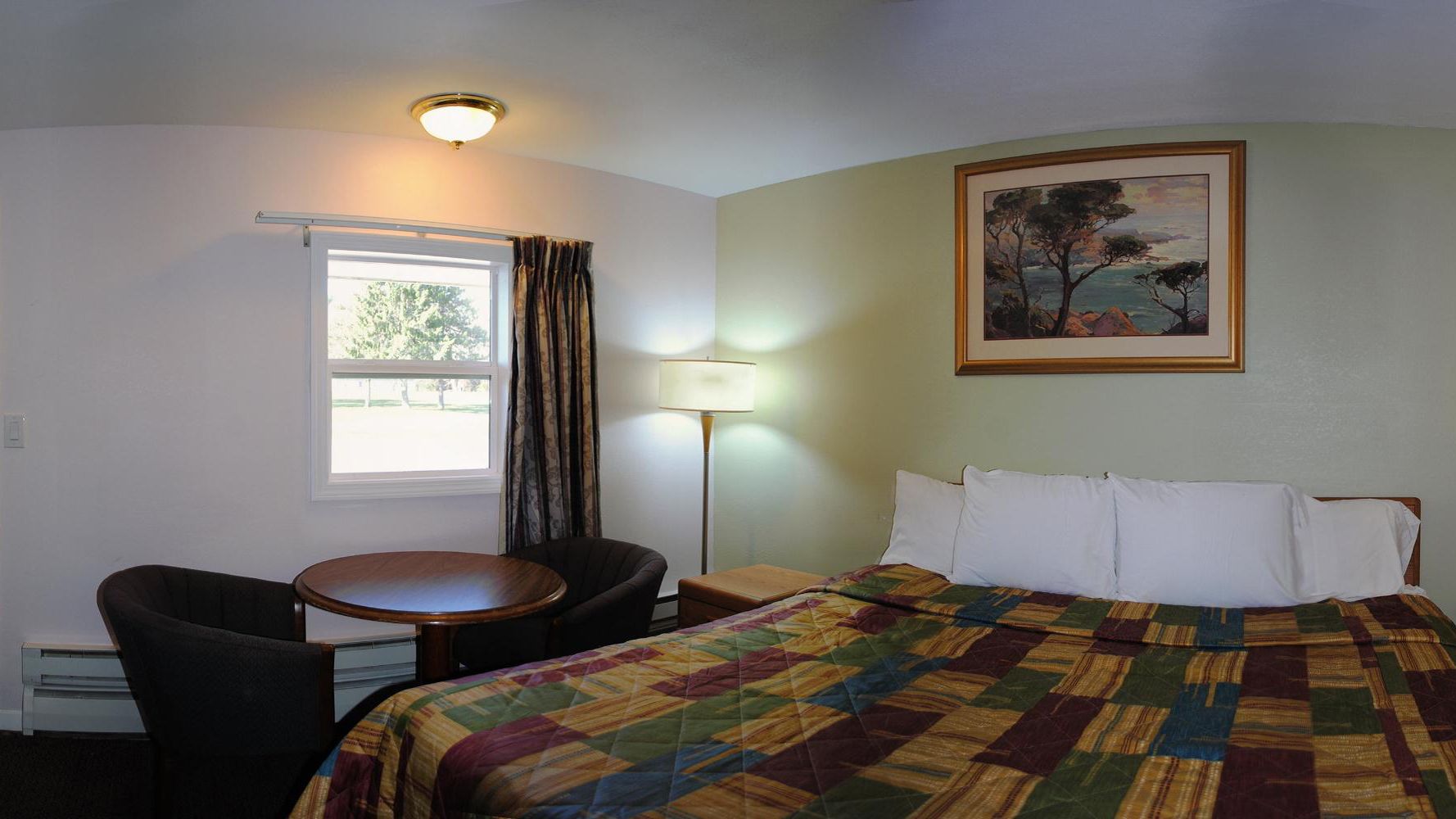 Una habitación de hotel con una cama, un escritorio, una silla, una lámpara y un cuadro en la pared.