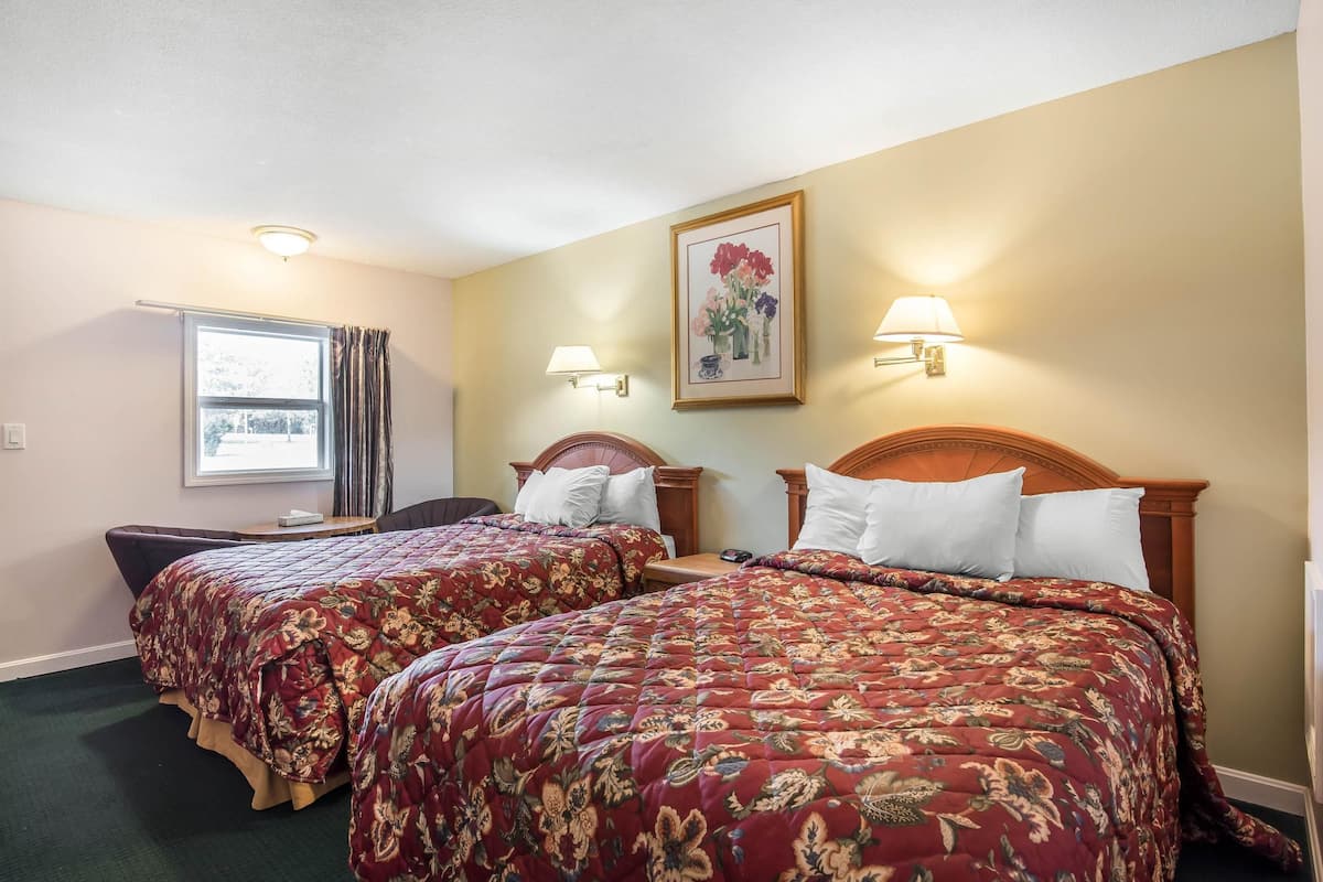 Quarto de hotel com duas camas, cada uma com roupa de cama estampada com flores, uma janela com cortinas e luminárias fixadas na parede.