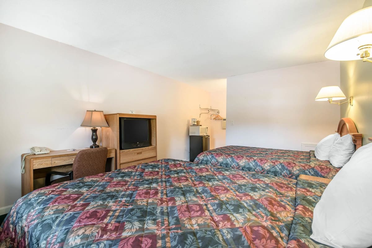 Quarto de hotel com duas camas, uma escrivaninha com abajur, televisão e uma pequena mesa com telefone.