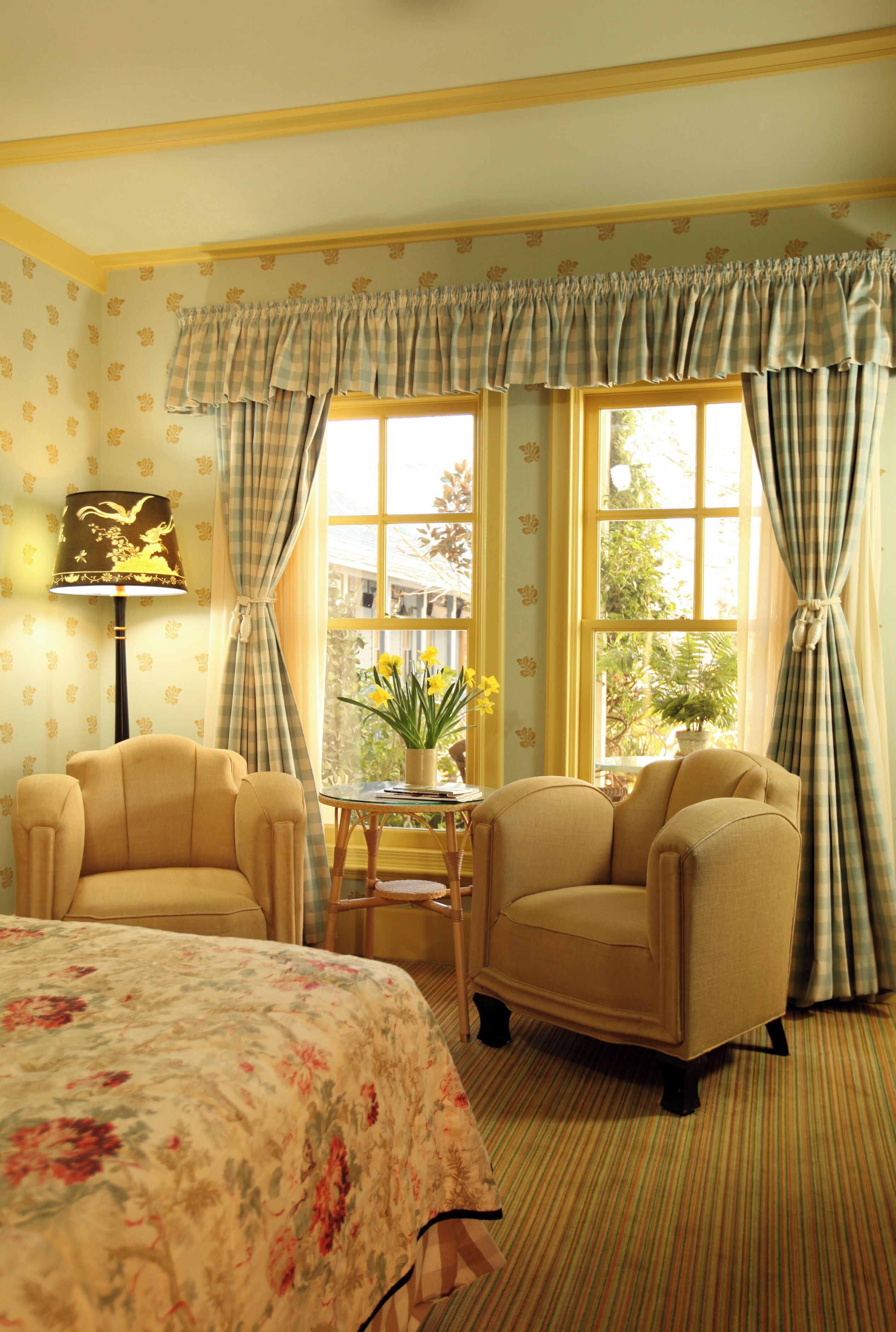 A room with two armchairs, a small table with a vase of flowers, and a lamp.