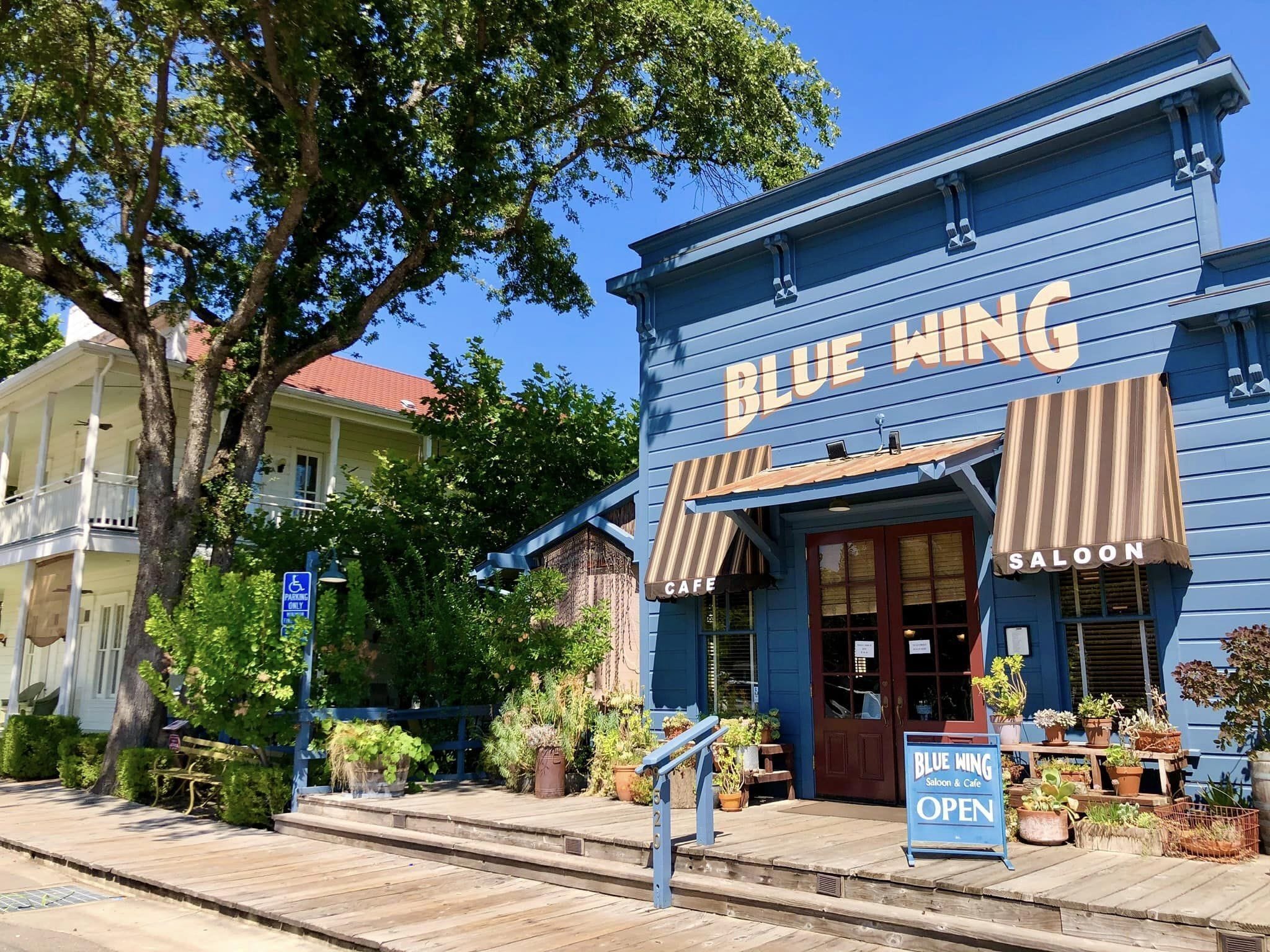 A Blue Wing Saloon & Cafe with a wooden deck and potted plants outside.