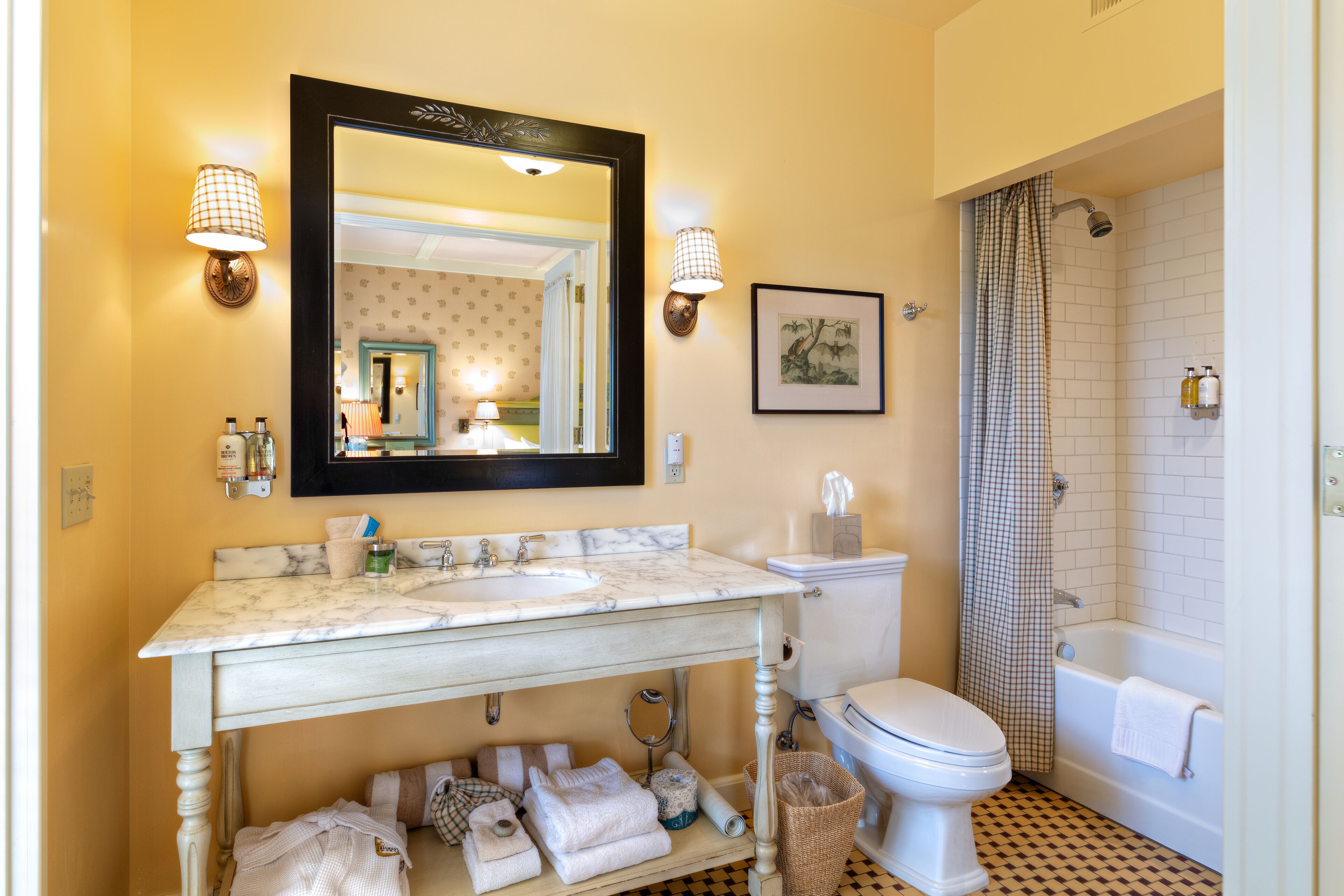 Une salle de bain avec un lavabo en marbre, des toilettes, une douche avec un rideau à carreaux et un tableau encadré au mur.