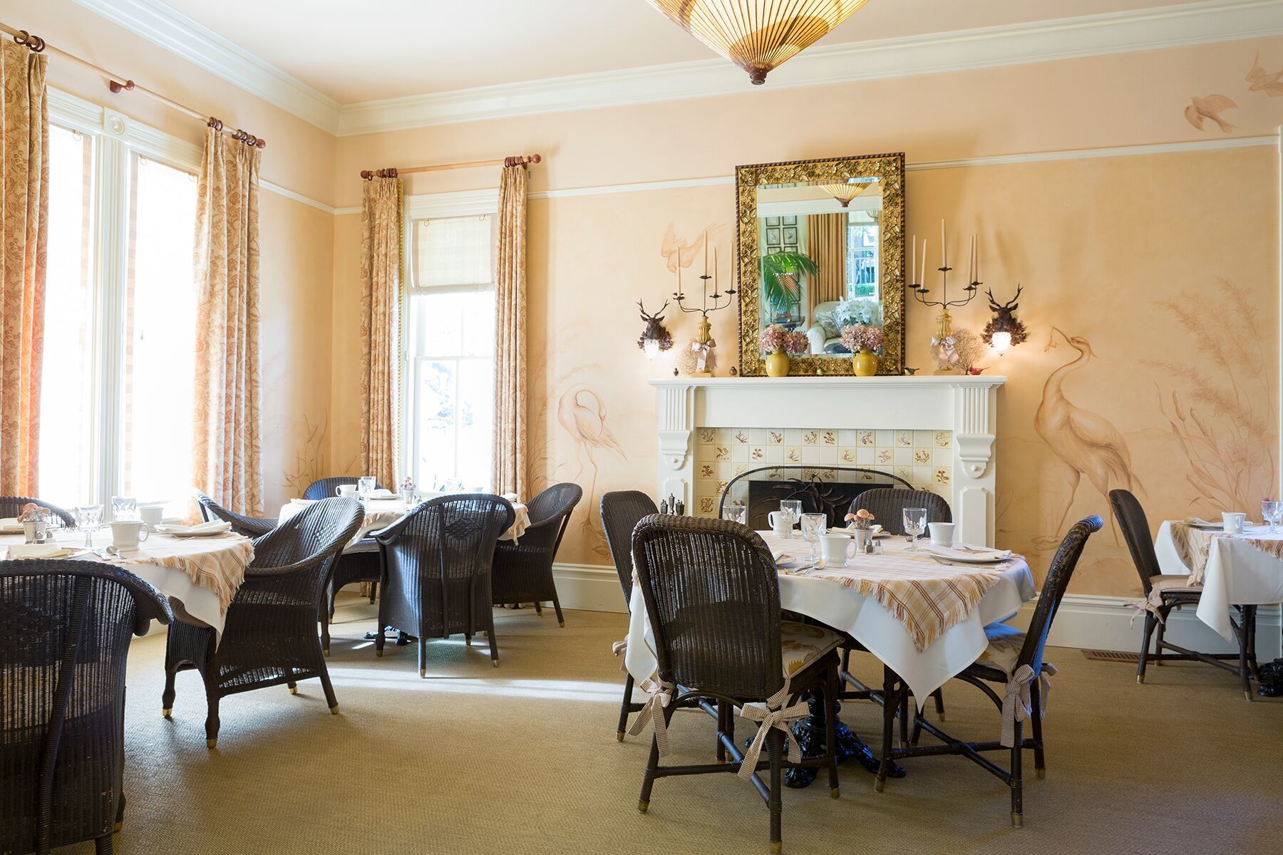 A dining room with multiple tables and chairs, a fireplace, and a large mirror above it.