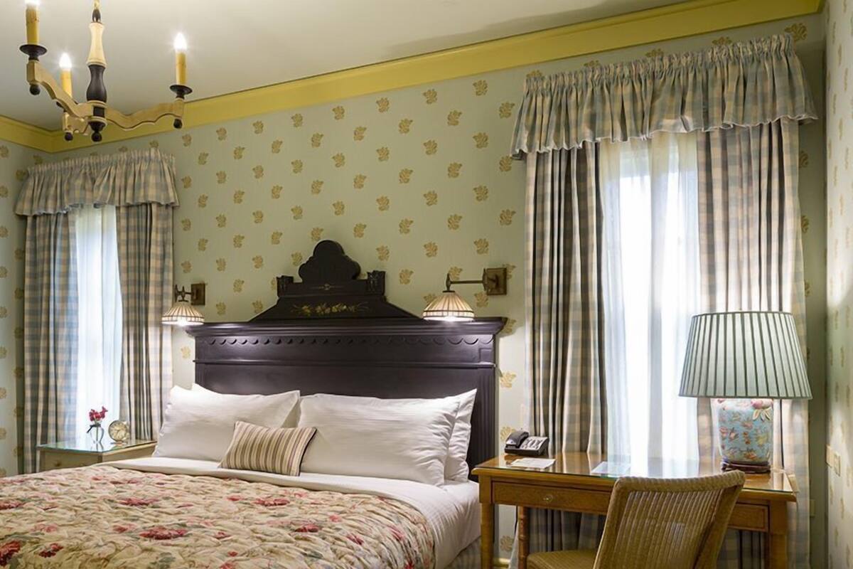 A hotel room with a large bed, a wooden headboard, a desk with a chair, and curtains.