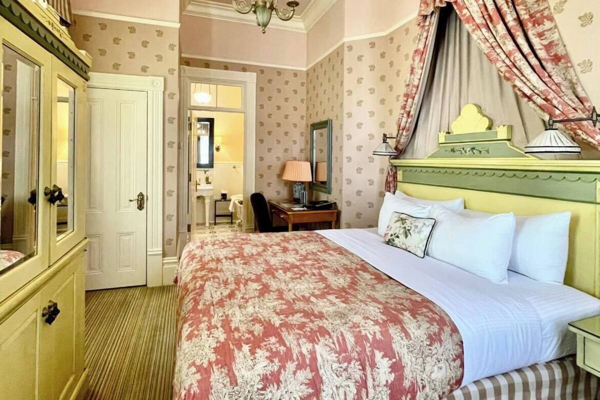 A bedroom with a large bed, a vanity with a mirror, a chandelier, and a canopy bed.