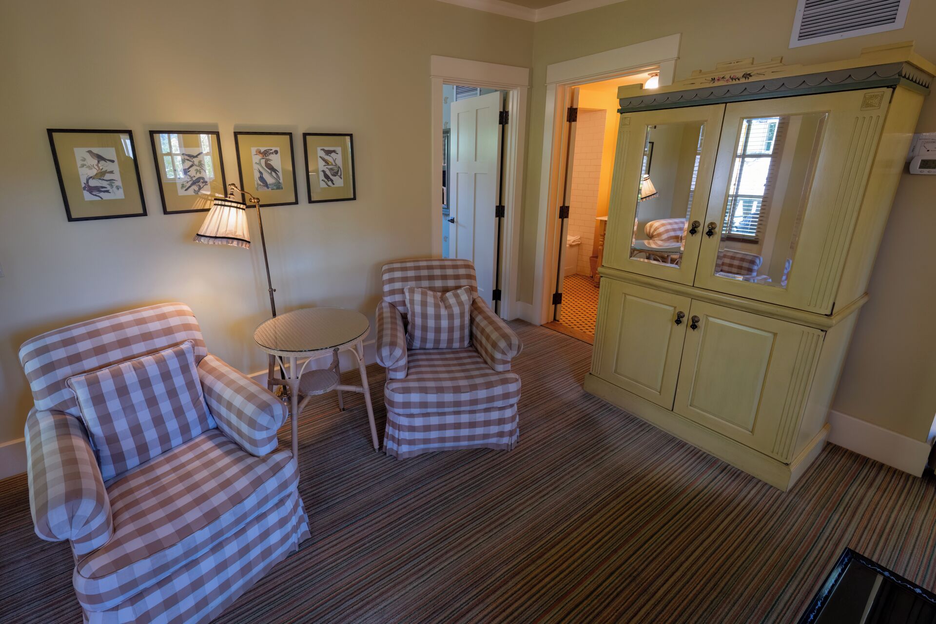 A room with two checkered armchairs, a small round table, and a cream-colored cabinet with glass doors.