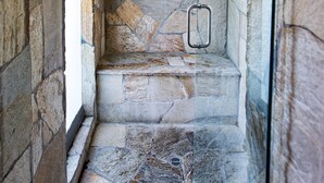 Ein Badezimmer mit Steinwänden, einem Duschbereich, einer Dekoration an der Wand und einer Glasdusche.