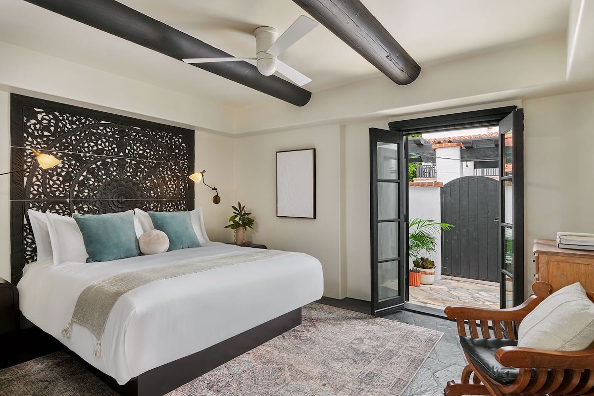 A bedroom with a bed, a ceiling fan, a wooden bench, and a door leading to a balcony.