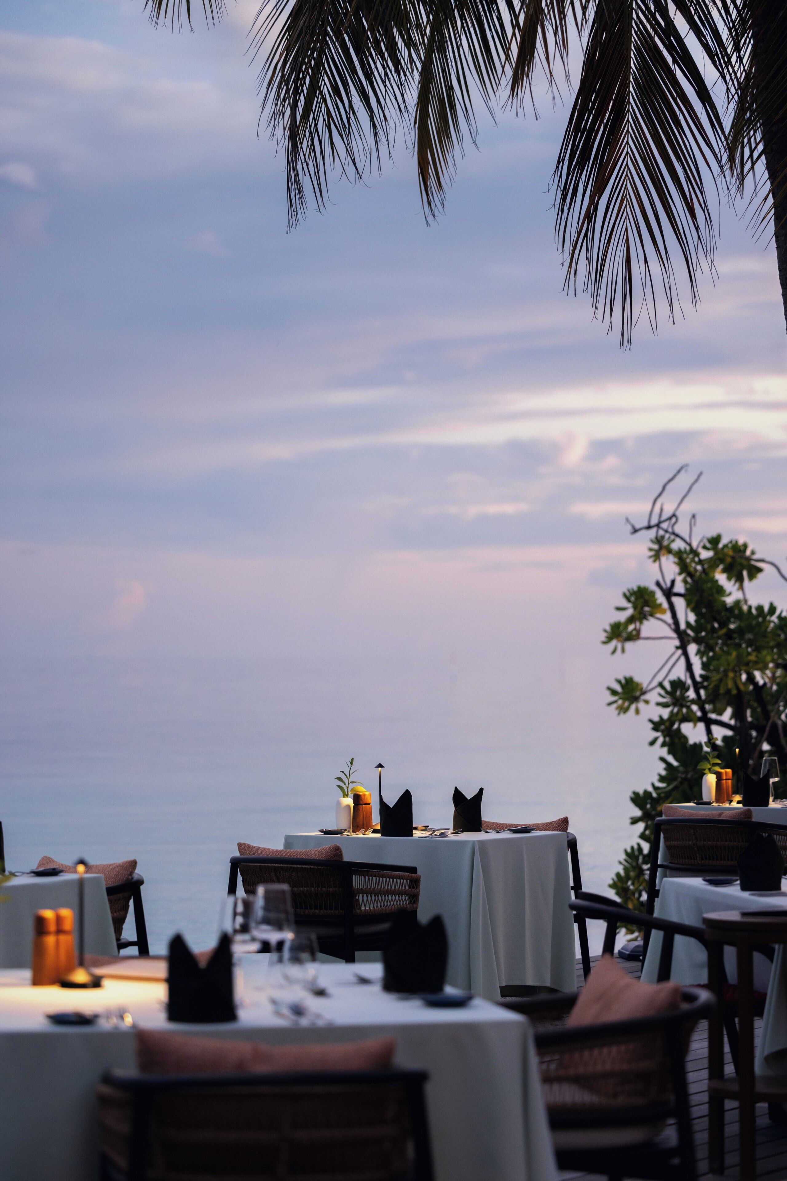 An outdoor dining area with tables set for two, overlooking a body of water.
