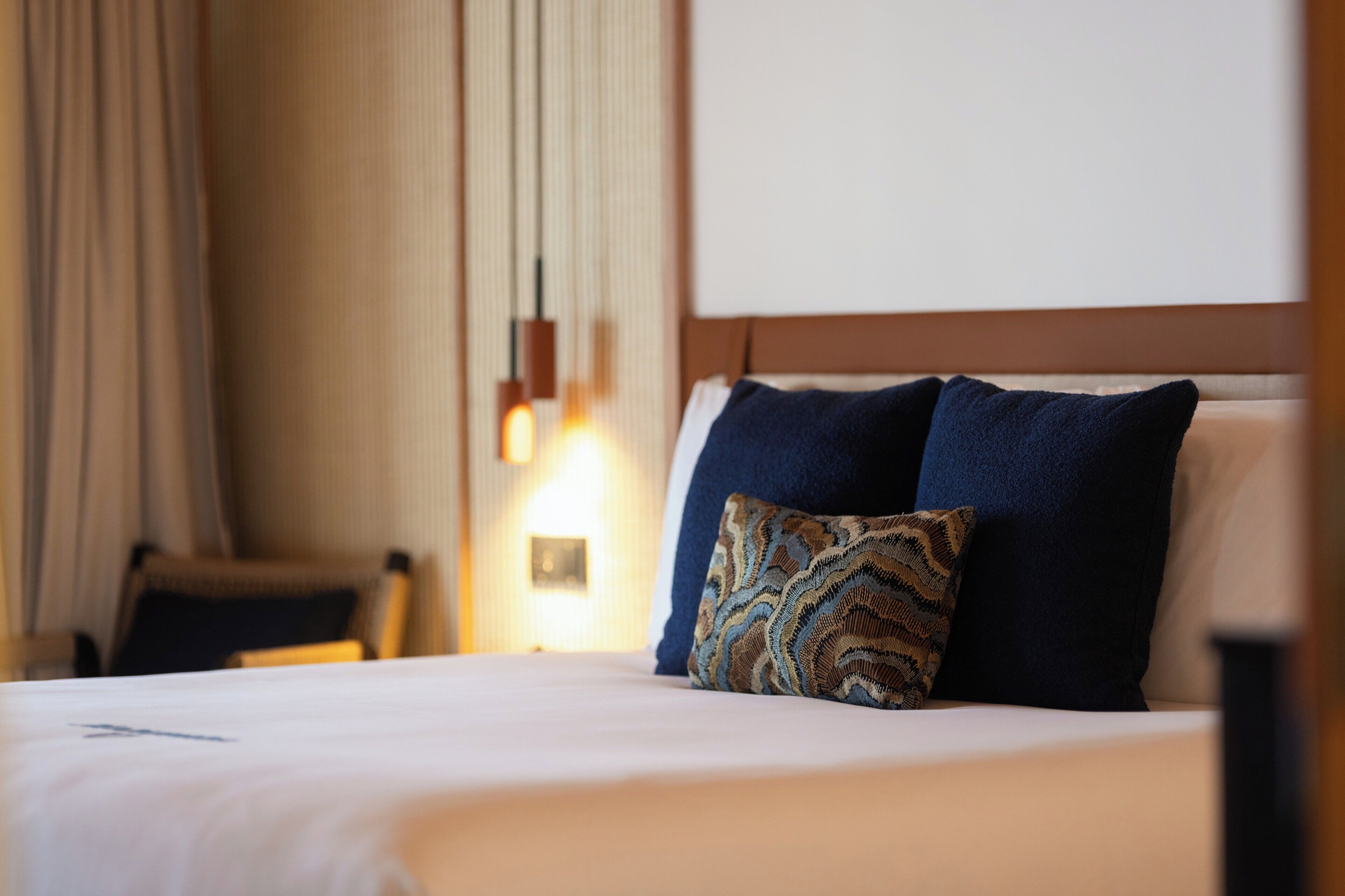 A hotel room with a bed, a chair, and a wall-mounted light fixture.