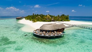 An overwater bungalows with thatched roofs, white sandy beaches, clear turquoise waters, and a pier connecting to a lush island with palm trees. - V Villas Maldives at Mirihi - MGallery Collection (Mirihi)