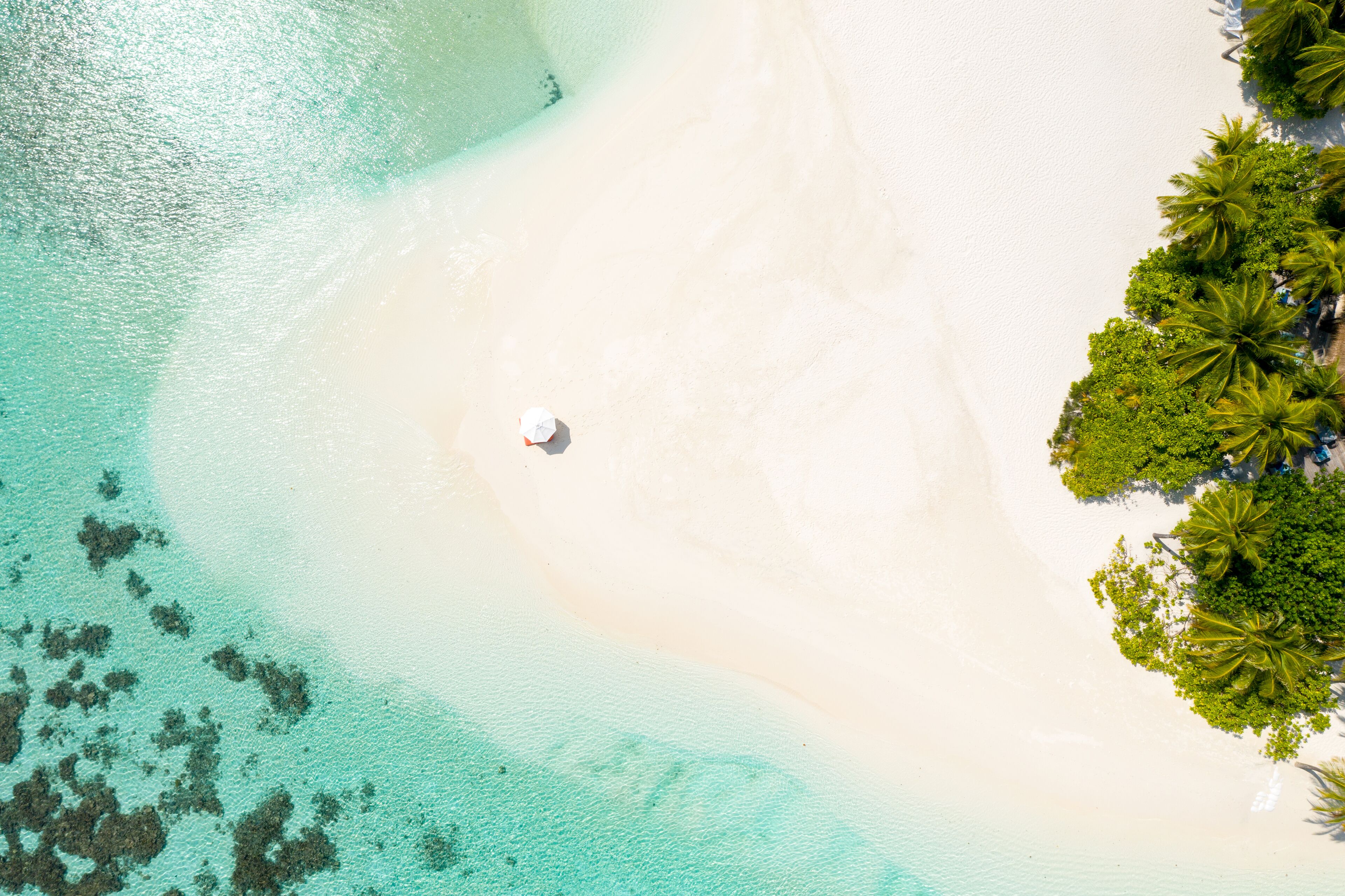 An aerial view of a beach with clear turquoise waters, white sand, and a small white object on the shore.