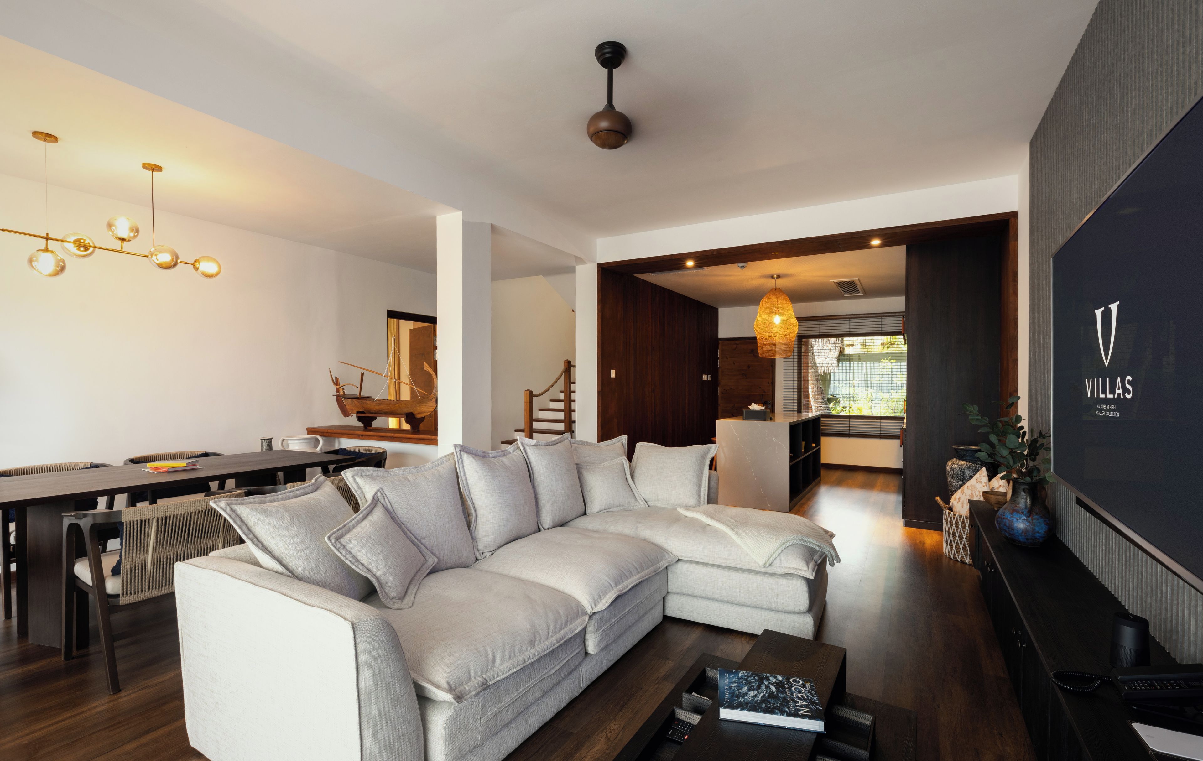 Una sala de estar moderna con un sofá seccional, un comedor con una mesa larga y una cocina al fondo.
