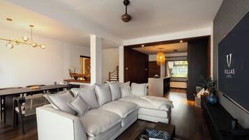 Una sala de estar moderna con un sofá seccional, un comedor con una mesa larga y una cocina al fondo.