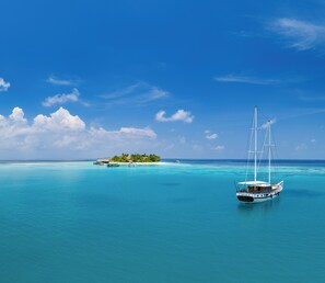 A clear blue sea with a sailboat, a small island with buildings, and a clear sky. - V Villas Maldives at Mirihi - MGallery Collection (Mirihi)