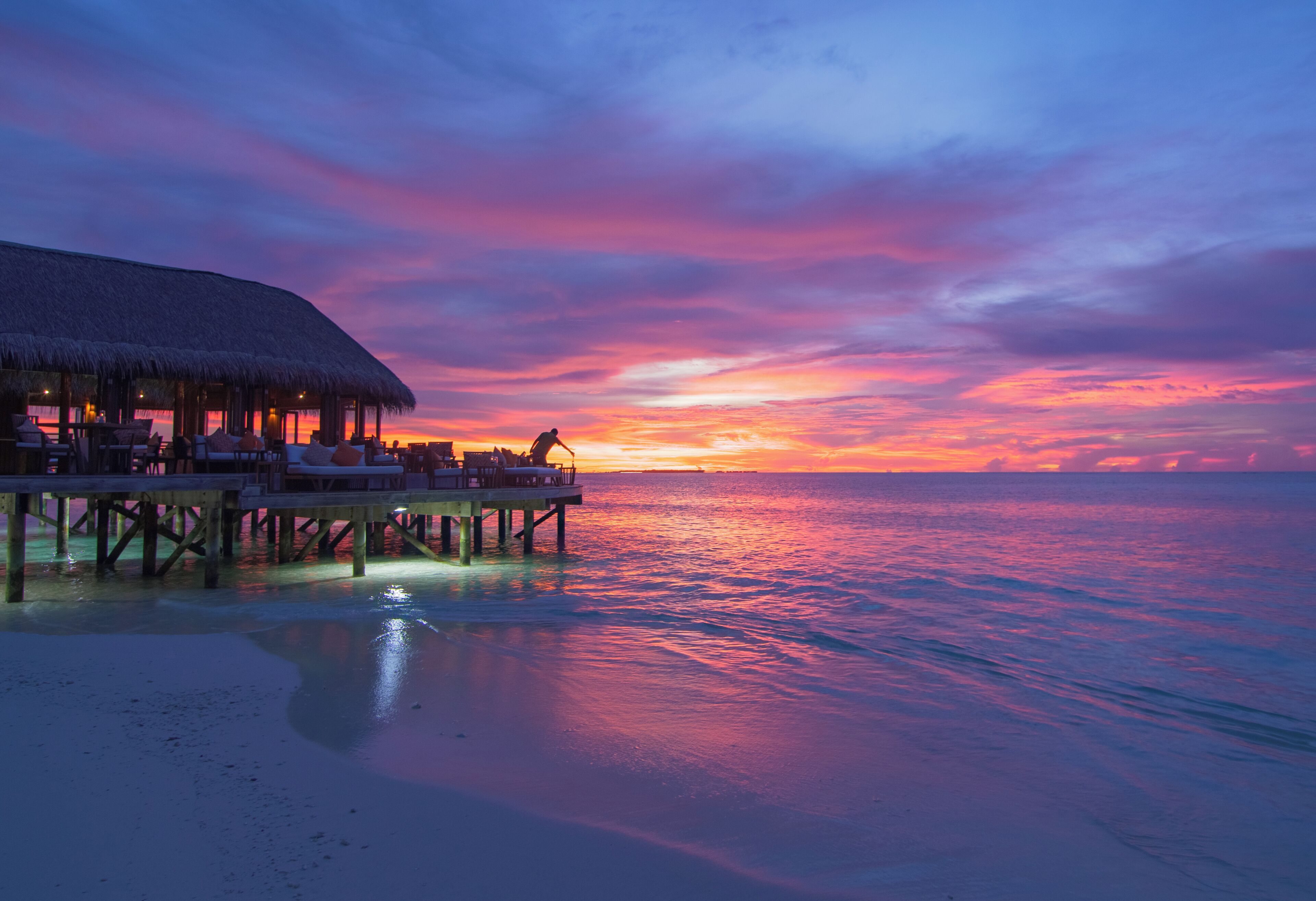 A beachside resort with a thatched-roof structure, lounge chairs, and a view of the ocean.