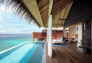 An infinity pool with a clear view of the ocean, a wooden deck, a thatched roof, and a modern interior with a bed and seating area. - V Villas Maldives at Mirihi - MGallery Collection (Mirihi)