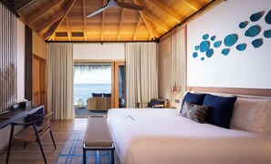 Habitación de hotel con cama, escritorio, silla, banco y vista al océano.