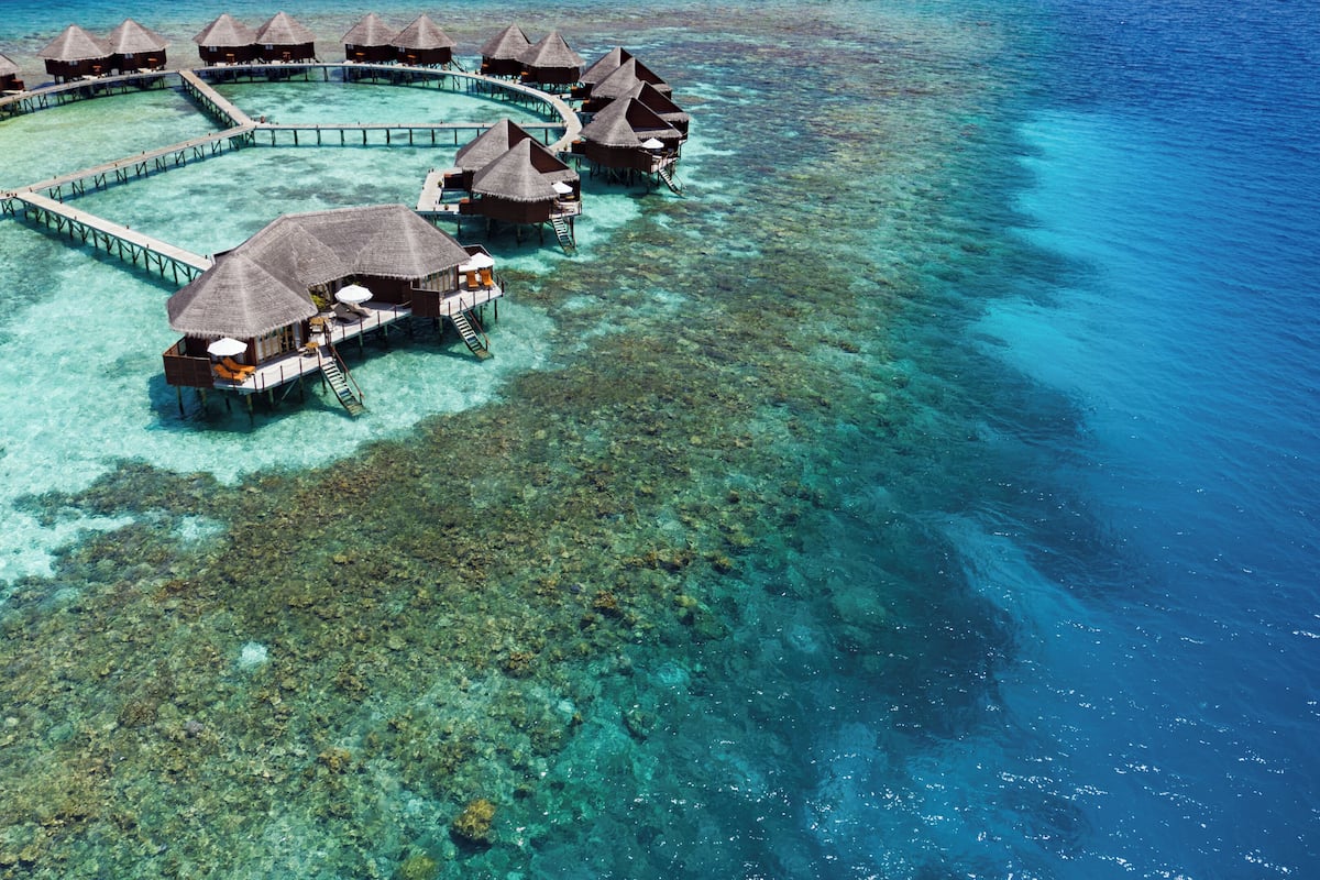 An aerial view of overwater bungalows with clear blue water, connected by walkways.