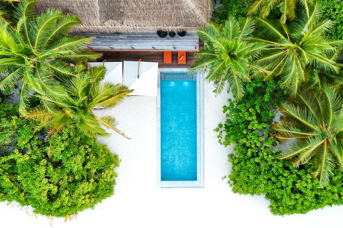 An aerial view of a resort with a swimming pool surrounded by lush greenery and a thatched-roof structure.