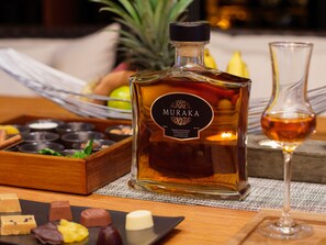 A bottle of Muraka liquor, a glass of whiskey, and assorted chocolates on a wooden tray.