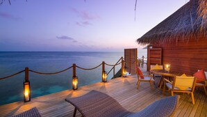 Terraza de madera con sillones y una mesa, con vista al océano al atardecer.