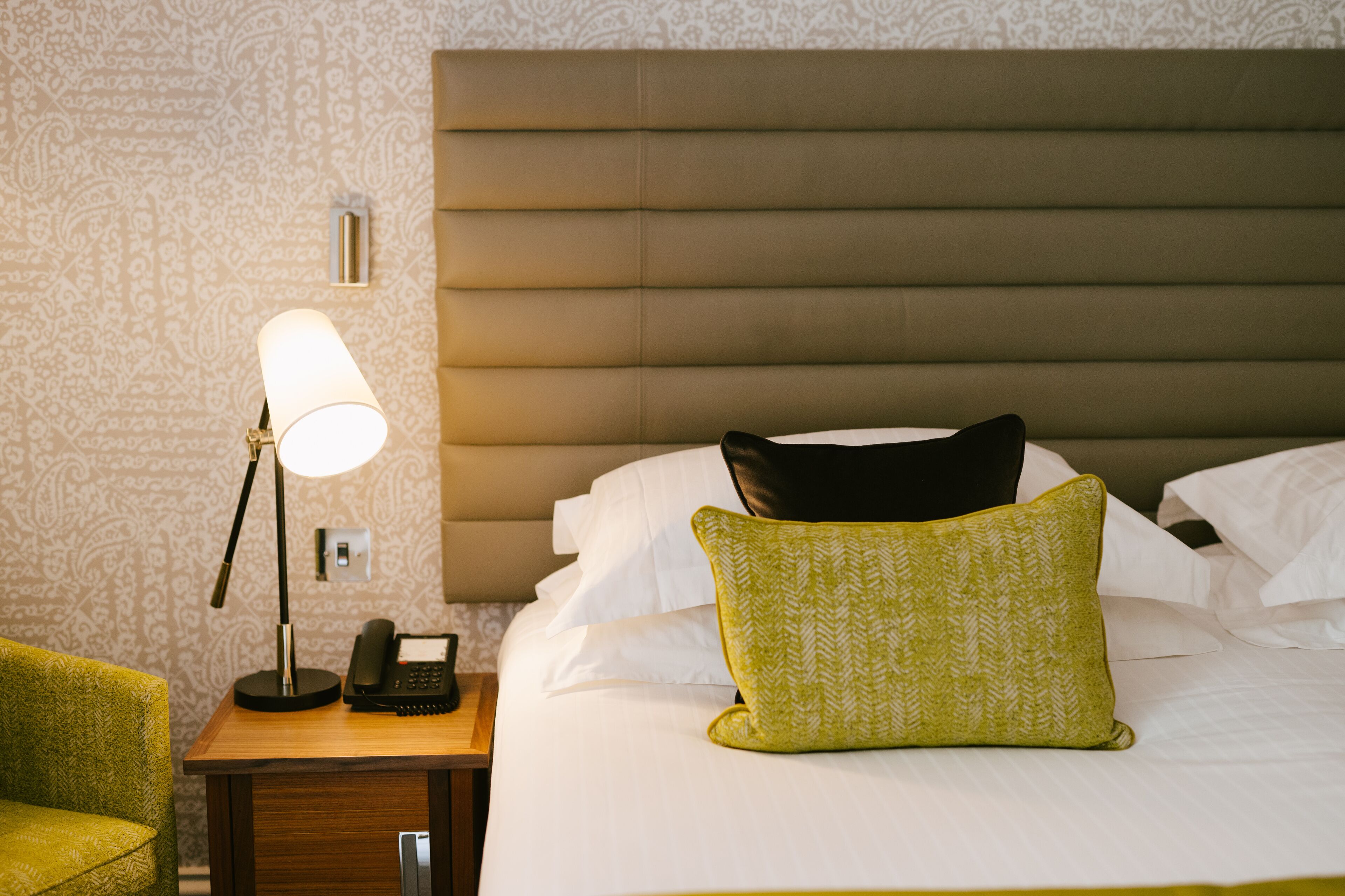 A neatly made hotel room with a bed, a bedside lamp, a telephone, and a small table.