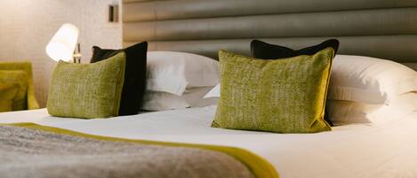 A neatly made bed with a grey headboard and green pillows.