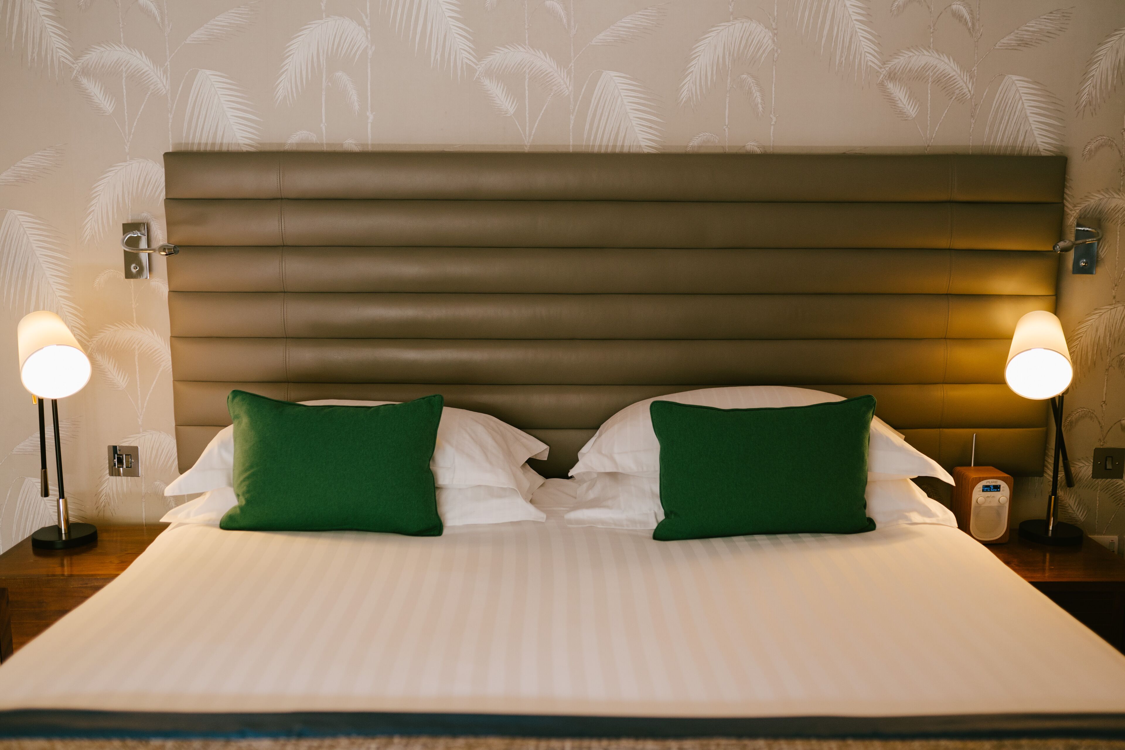 A neatly made bed with green pillows, a headboard, and bedside lamps.