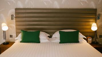 A neatly made bed with green pillows, a headboard, and bedside lamps.