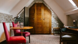 A cozy attic room with a wooden wardrobe, a dining table with chairs, and a radiator. - Jesmond Dene House (Newcastle-upon-Tyne)