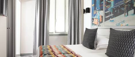 Habitación de hotel con cama, cortinas grises, colcha estampada y una pared con obras de arte.