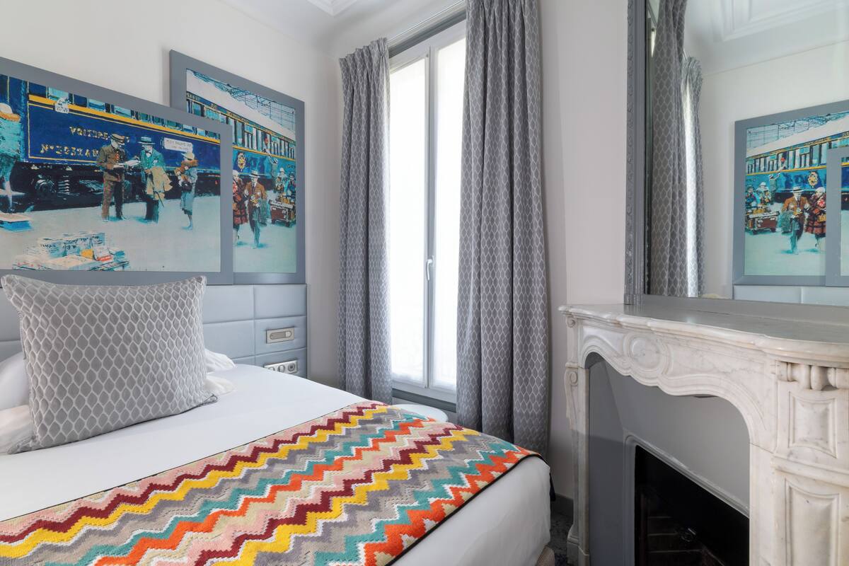 A hotel room with a bed, a fireplace, and artwork on the walls.