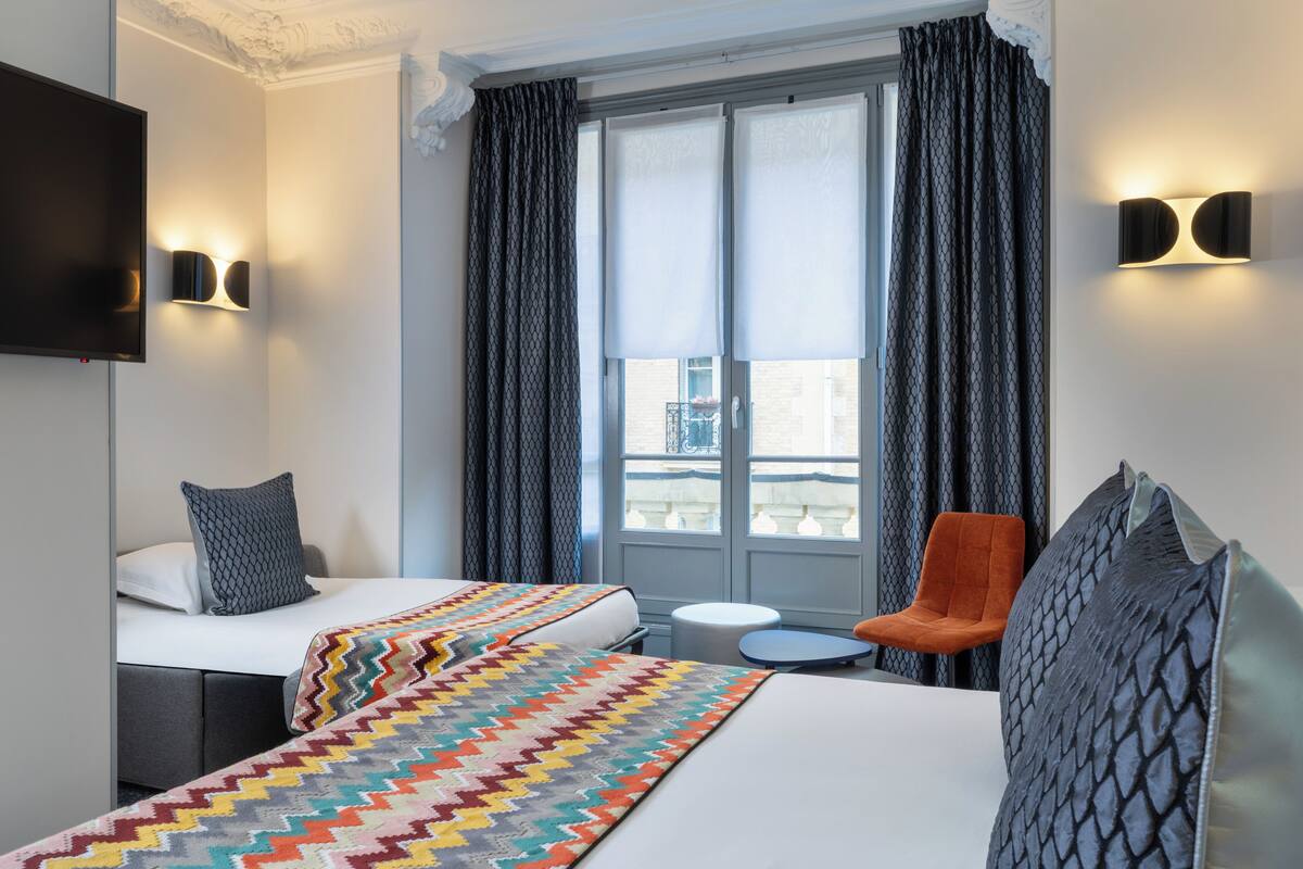 A hotel room with two beds, a TV, a small round table, and a chair.