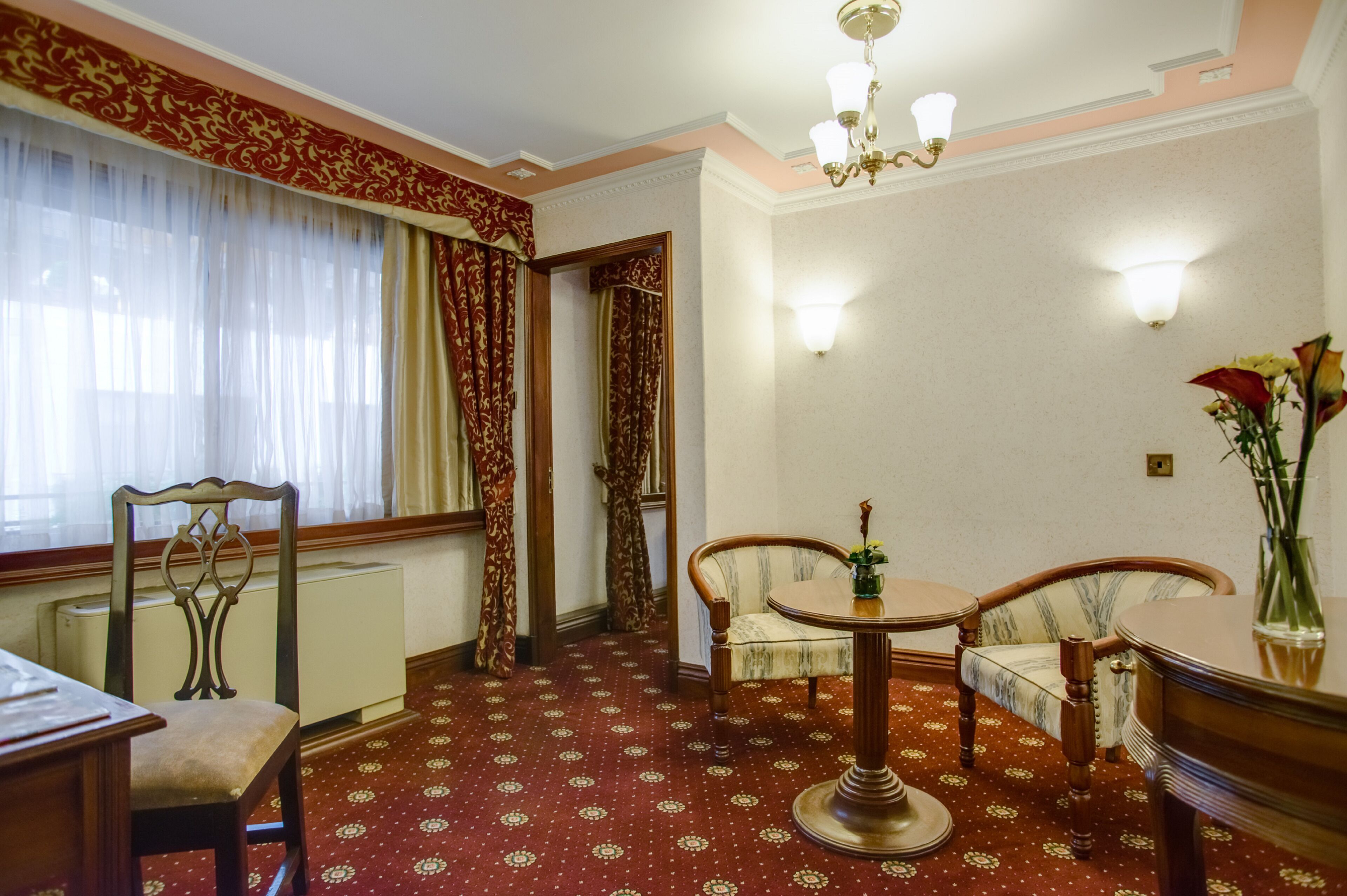Una habitación con alfombra estampada, una mesa de comedor con sillas, un radiador y una ventana con cortinas.