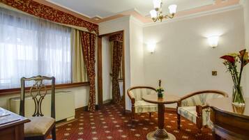 Una habitación con alfombra estampada, una mesa de comedor con sillas, un radiador y una ventana con cortinas.