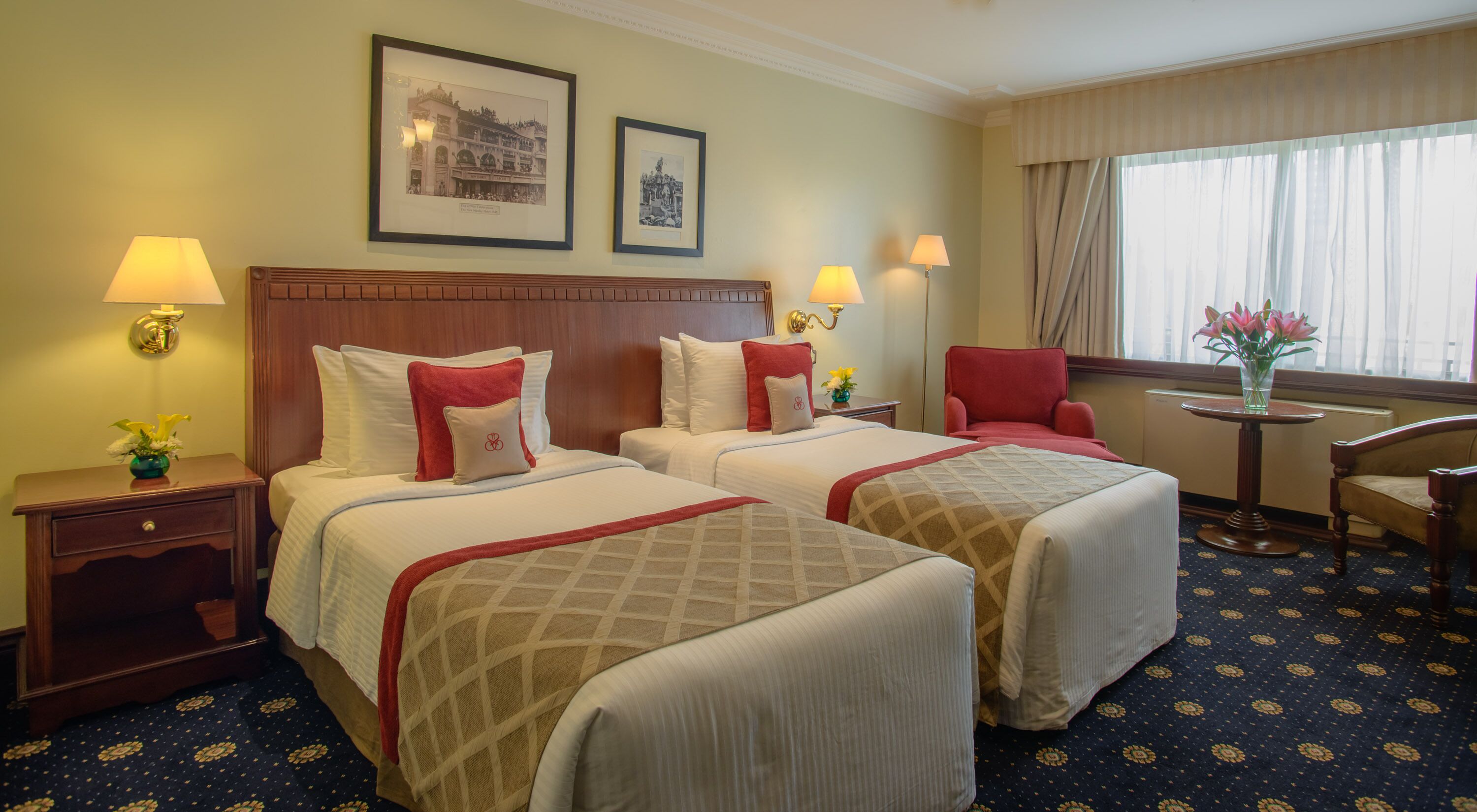 A hotel room with two beds, a desk, a chair, and a window with curtains.