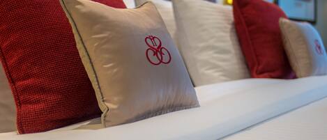 Una cama bien hecha con una variedad de almohadas, algunas con un logotipo rojo.