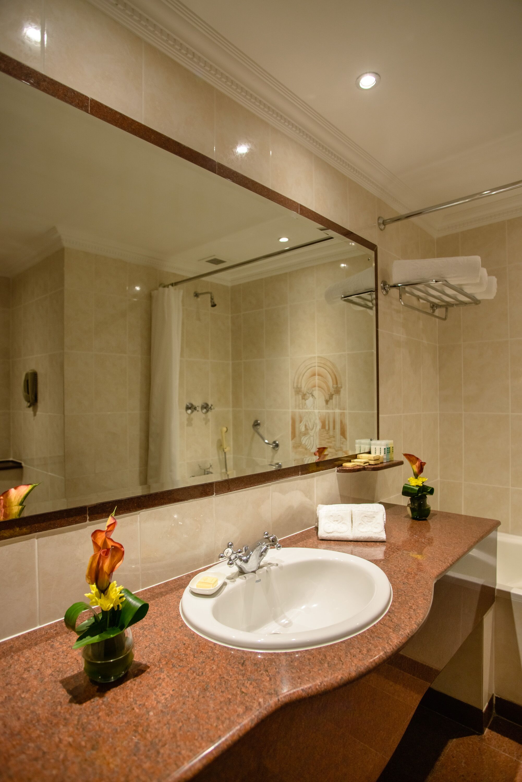 A bathroom with a marble sink, a large mirror, a shower, and a towel rack.
