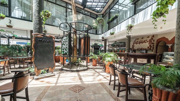 A spacious indoor area with multiple seating arrangements, a central decorative structure, and hanging plants. - Sarova Stanley Hotel, Nairobi (Nairobi)