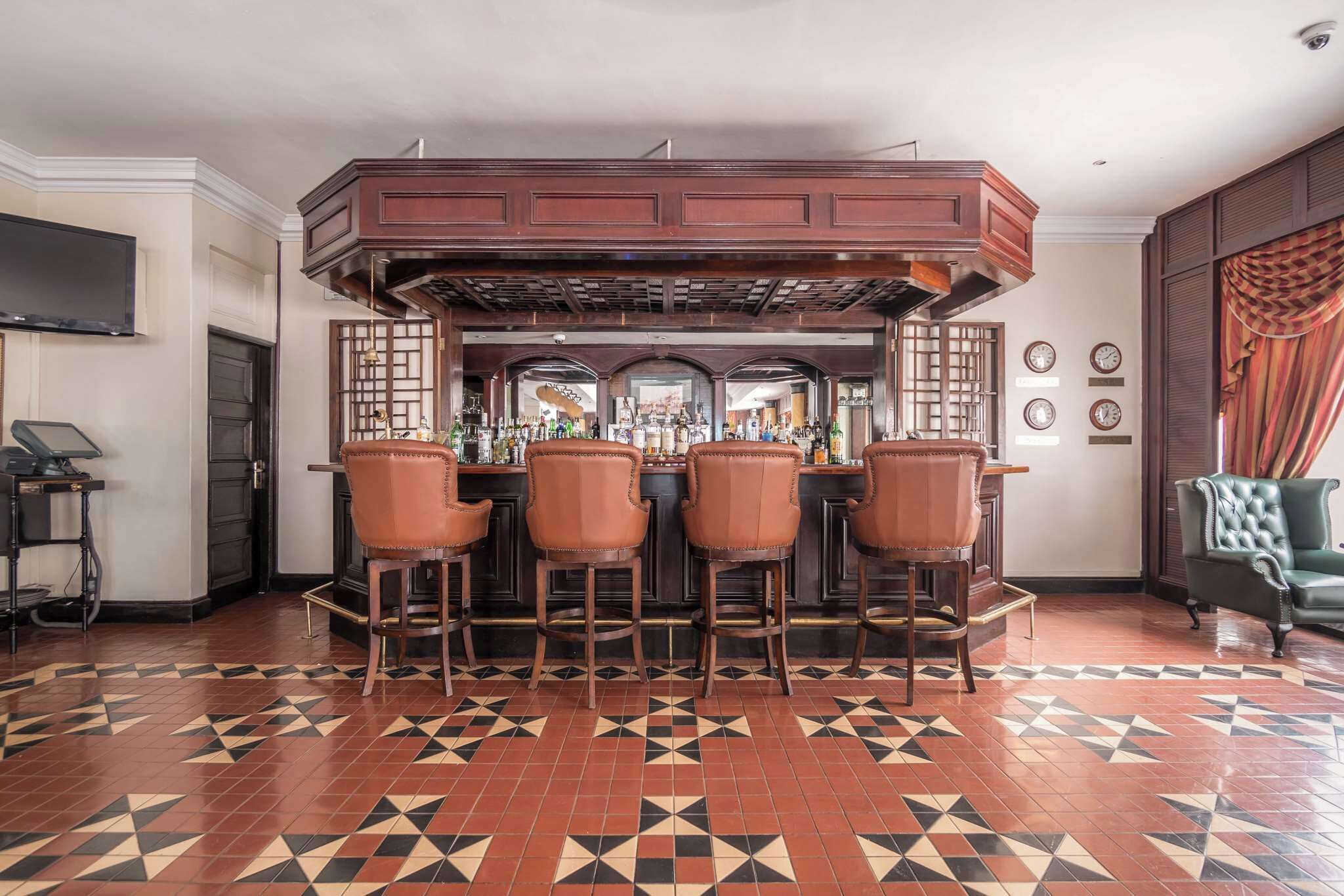 A bar area with four stools, a bar counter, and a television mounted on the wall.