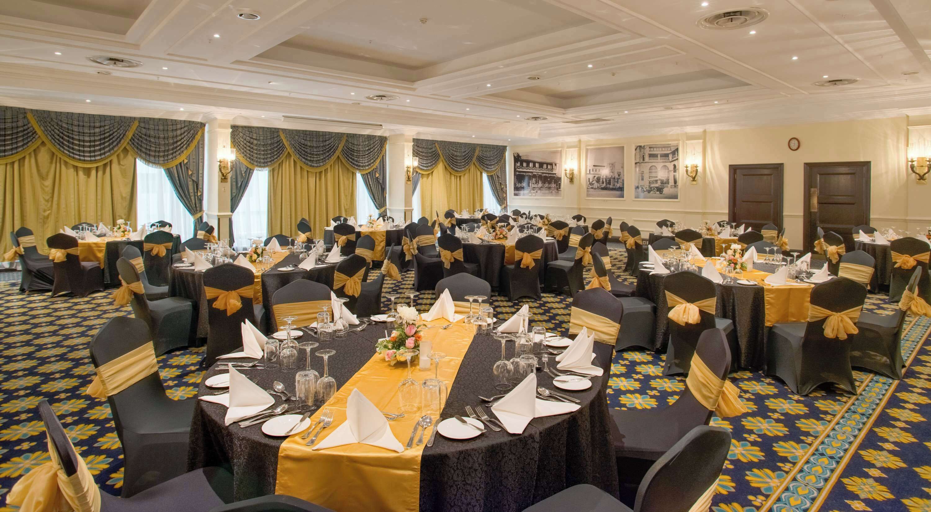 A banquet hall with round tables, black chairs with gold sashes, and yellow tablecloths.