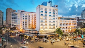 Un hotel a più piani dal design moderno, con balconi su ogni piano, un cortile centrale e un'area parcheggio con diverse auto.