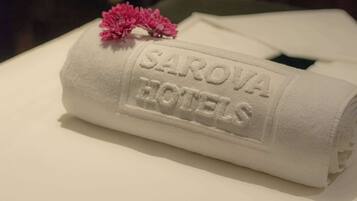 Une serviette blanche, soigneusement pliée et portant en relief l’inscription « SAROVA HOTELS », est posée sur un lit.